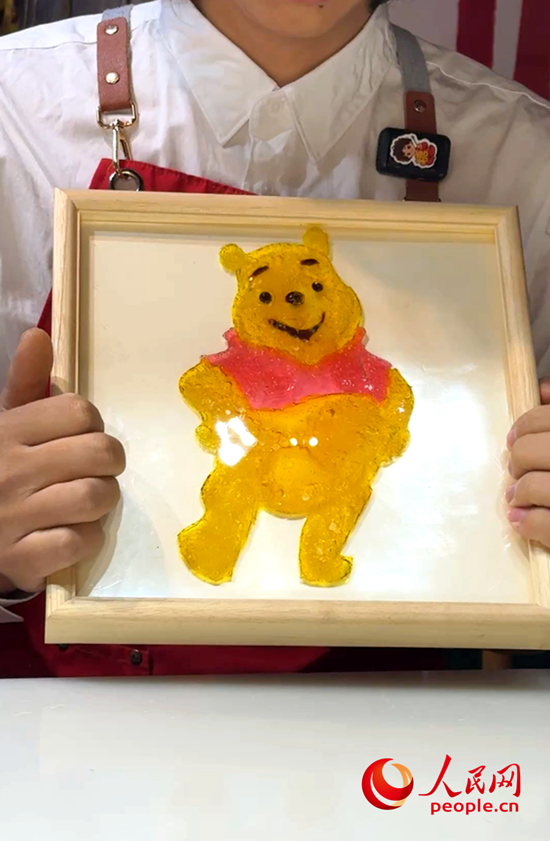 王岐洋向记者展示将糖画封入滴胶，制成的可悬挂墙面的艺术品。人民网记者 侯琳琳摄.jpg